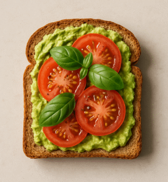 Imagen de una tostada de pan integral con aguacate, tomate y albahaca, iluminación natural, fondo neutro